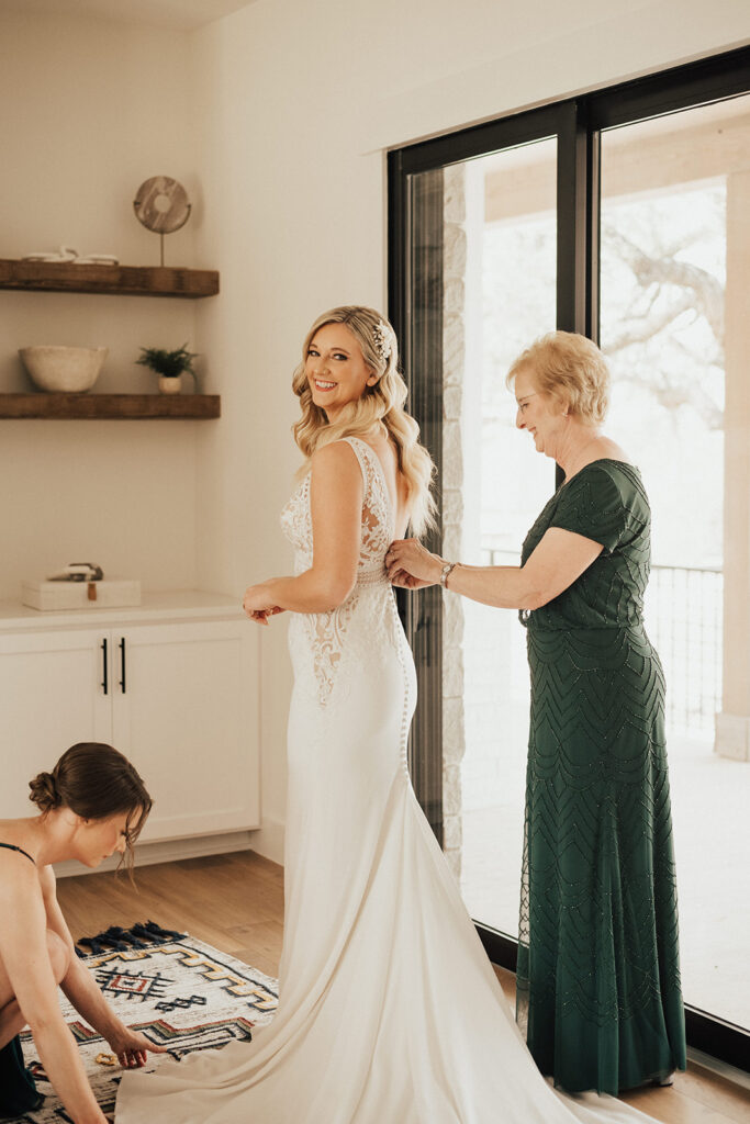 bride in deep neck wedding dress with lace elements getting into wedding dress with mother of the bride
