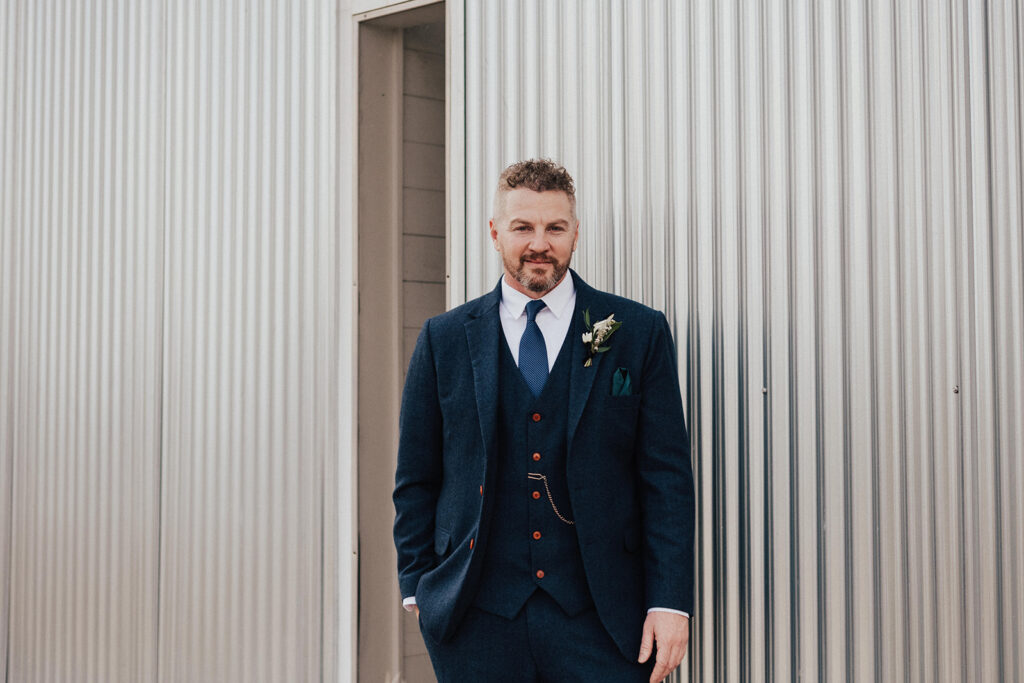 groom in navy blue suit with pocket watch stands in front of Prospect House before destination wedding