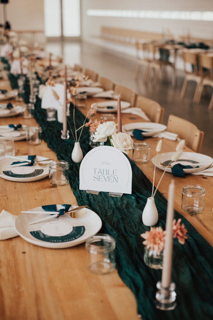 contemporary wedding reception with oak table and chairs, dark green gauze table runner and beige taper candles