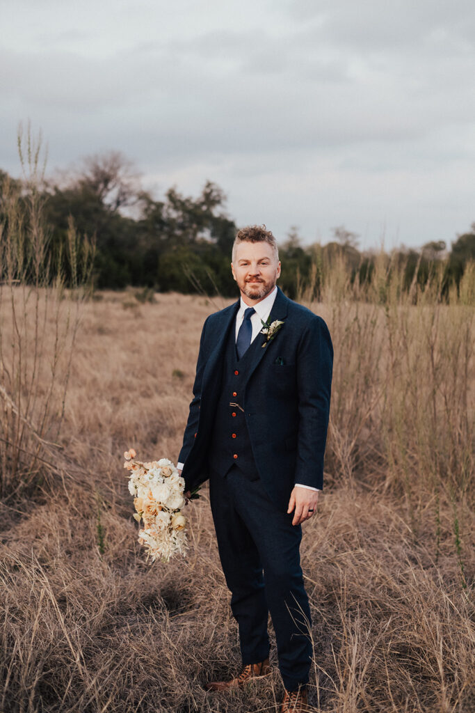 groom in navy blue suit and brown shoes holding bouquet