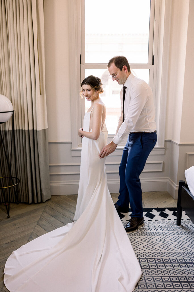 bride in minimalist wedding dress and groom in navy suit and black tie getting ready together