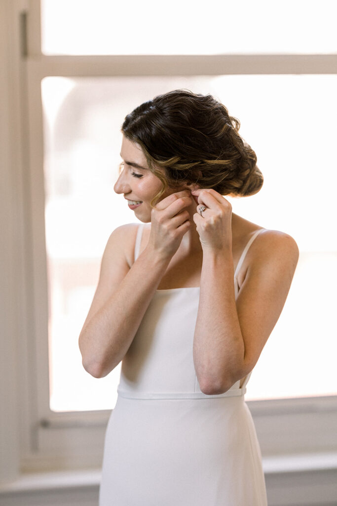 bride in minimalist wedding dress putting on earrings