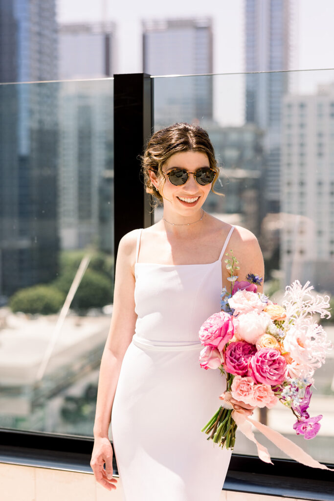  bride in minimalist wedding dress and colorful bridal bouquet with DTLA skyline in background