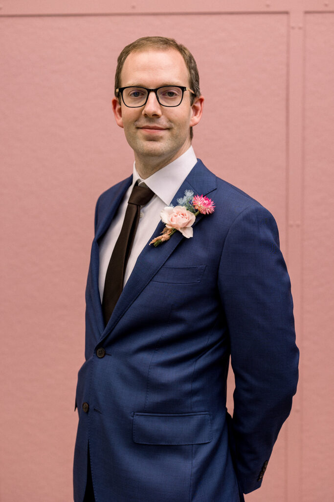 groom with glasses in dark blue suit and black tie with colorful boutonniere 