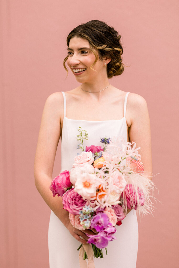 bride in minimalist wedding dress and colorful bouquet stand in front of pink keyhole wall at Grass Room DTLA