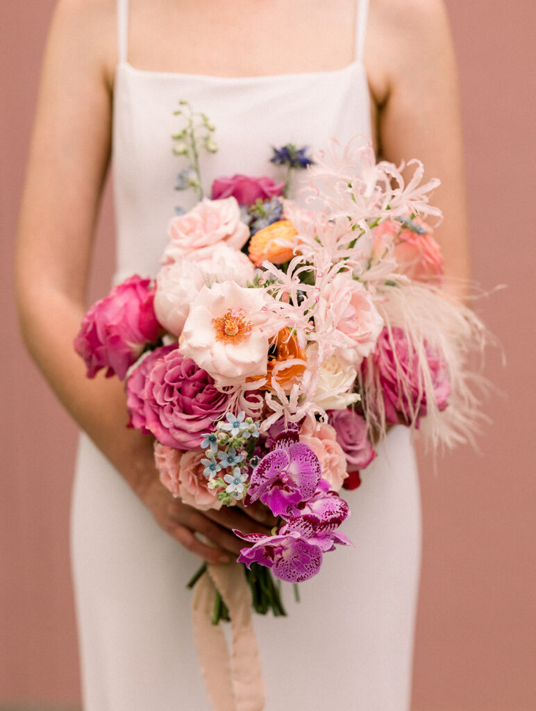 bride in minimalist wedding dress and colorful bouquet stand in front of pink keyhole wall at Grass Room DTLA