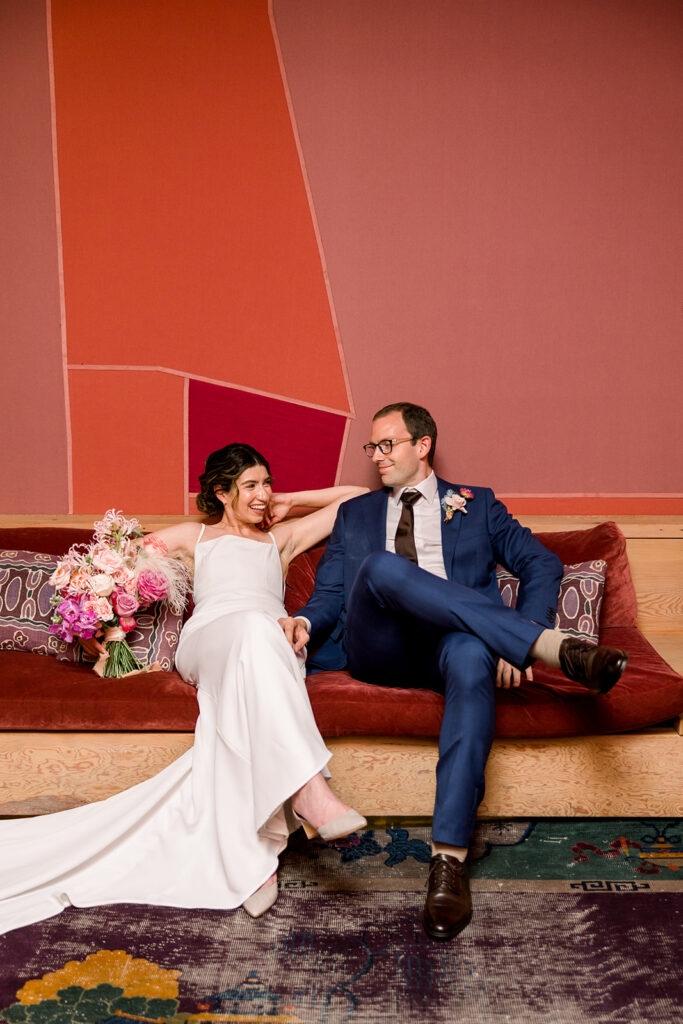 bride in minimalist wedding dress and  groom in dark blue suit sit in front of painted geometric wall at Grass Room DTLA