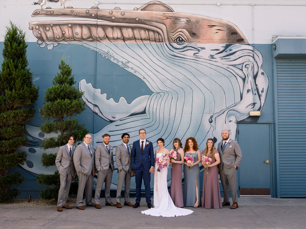 bride and groom stand with wedding party in front of whale mural at Grass Room DTLA