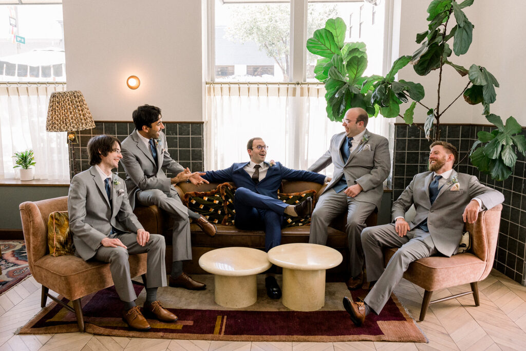 groom in dark blue suit sits with groomsmen in grey suits