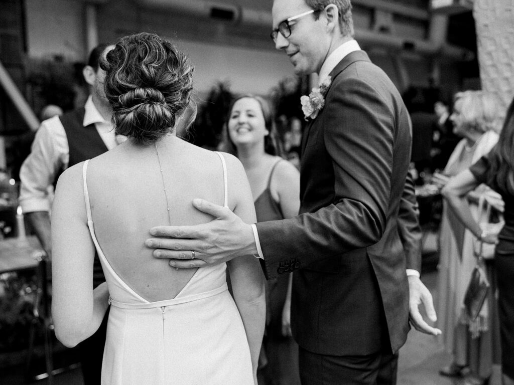 black and white photo of grooms hand on back of bride during cocktail hour