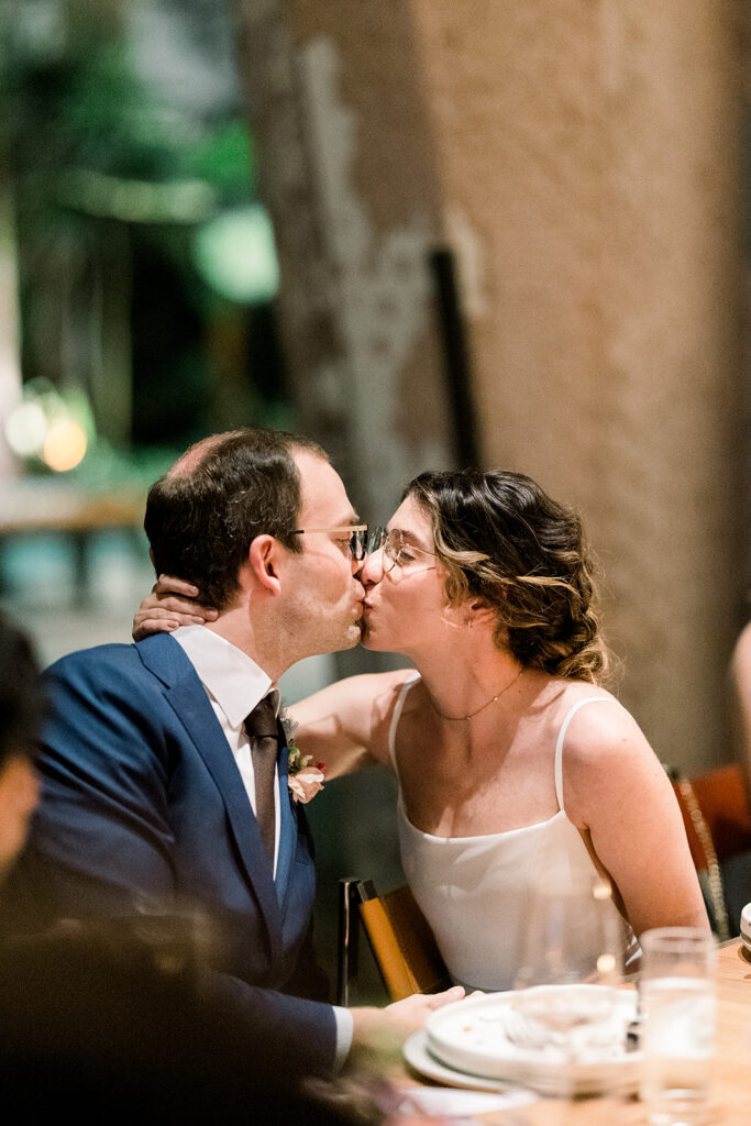 bride in glasses kissing groom in glasses during wedding reception 