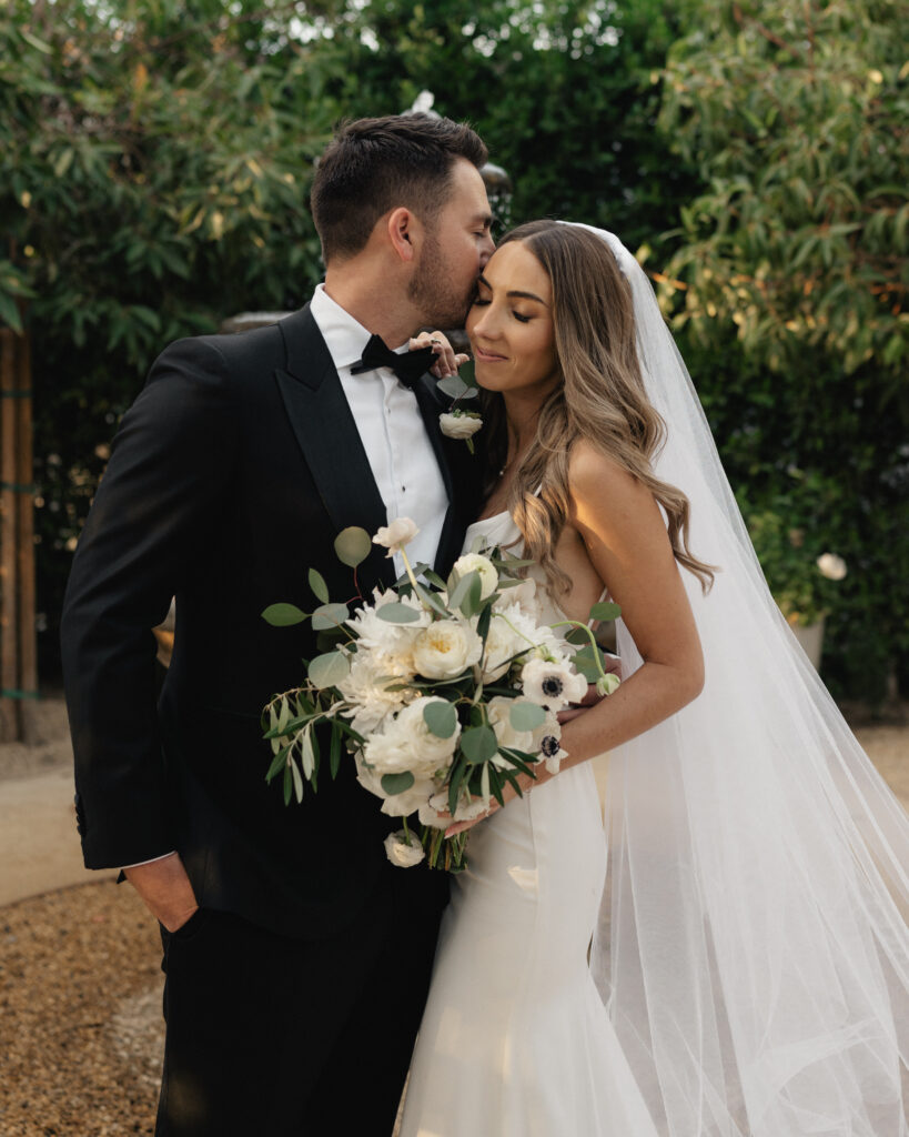 bride in modern minimalist wedding dress and cathedral veil with groom in classic black tuxedo suit 