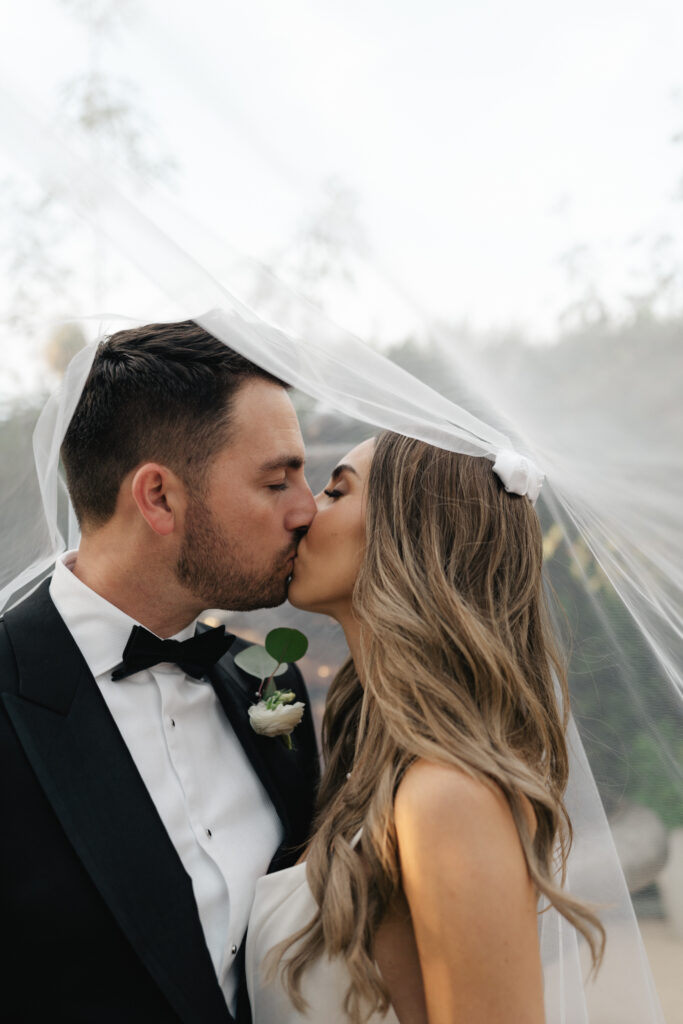 bride in modern minimalist wedding dress and cathedral veil with groom in classic black tuxedo suit 