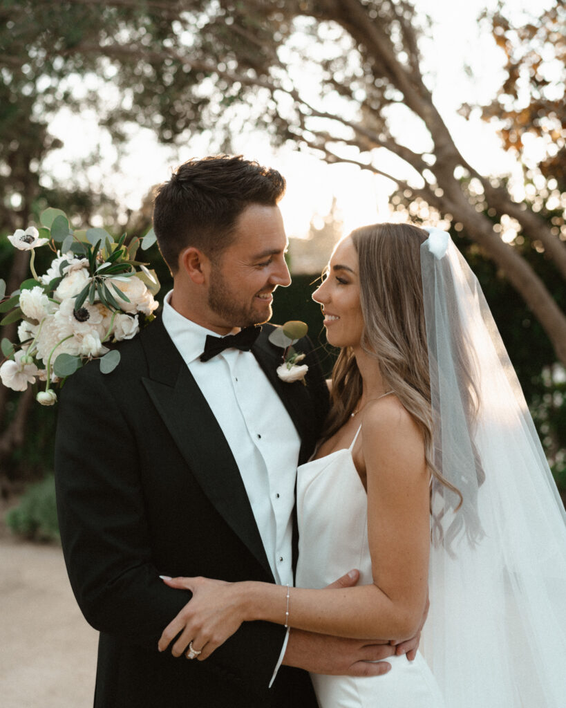 sunset photos with bride in modern minimalist wedding dress and cathedral veil with groom in classic black tuxedo suit 