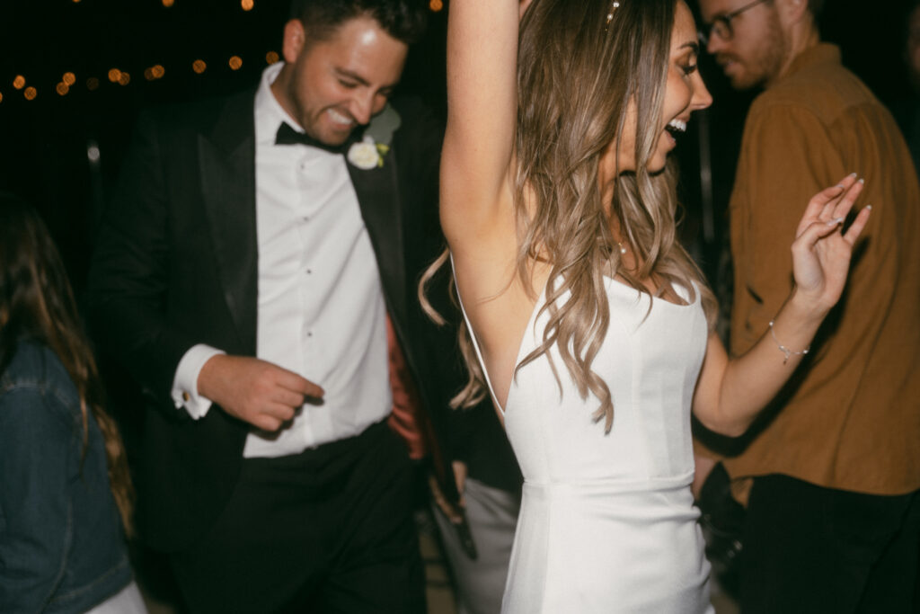 bride in modern minimalist wedding dress and groom in classic black tuxedo suit dance during wedding reception 