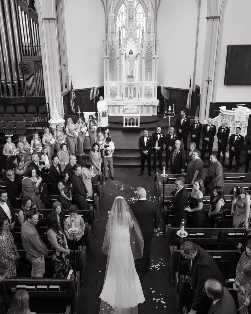 bride in cathedral veil walking down ceremony aisle during church wedding