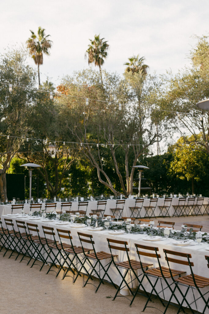 large elegant understated outdoor wedding reception with long tables in white linen, eucalyptus leaves and wooden patio chairs
