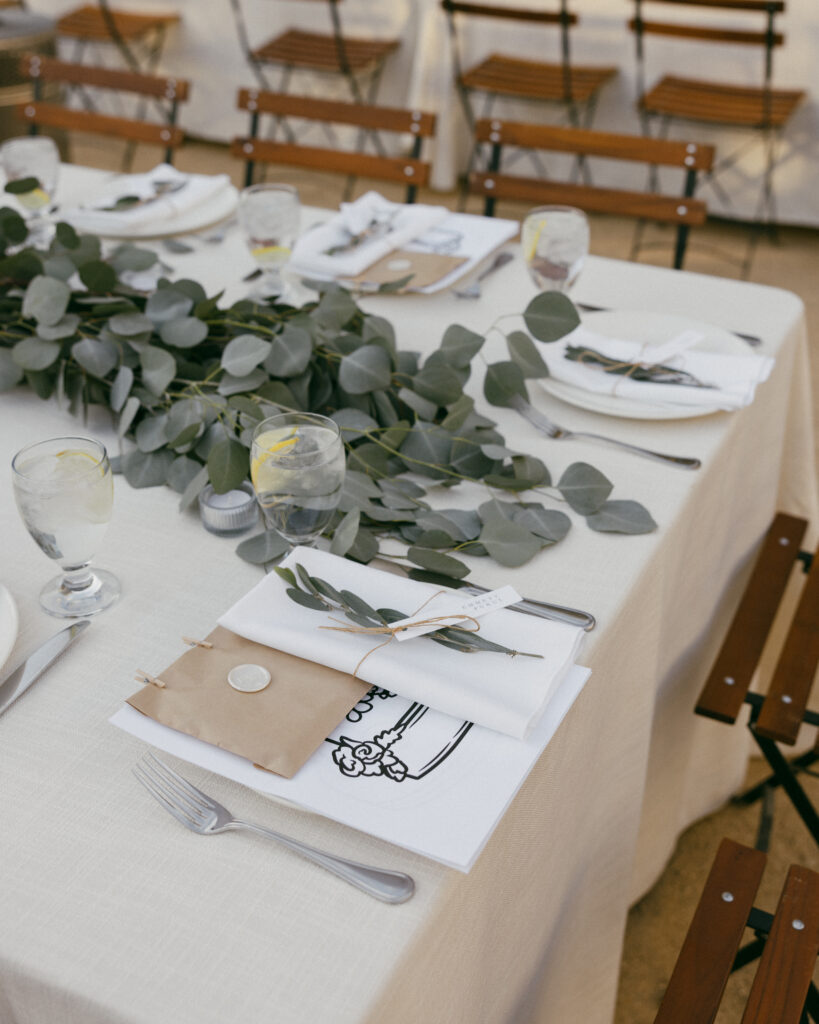 large elegant understated outdoor wedding reception with long tables in white linen, eucalyptus leaves and wooden patio chairs and coloring pages for kids table