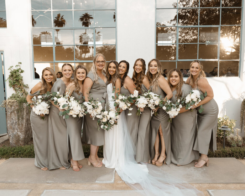 bride in minimalist modern wedding dress stands with bridesmaids in soft sage green mix matched dresses