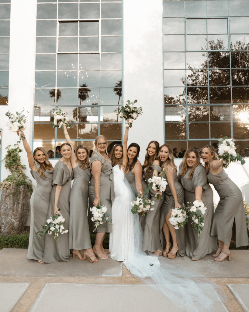 bride in minimalist modern wedding dress stands with bridesmaids in soft sage green mix matched dresses
