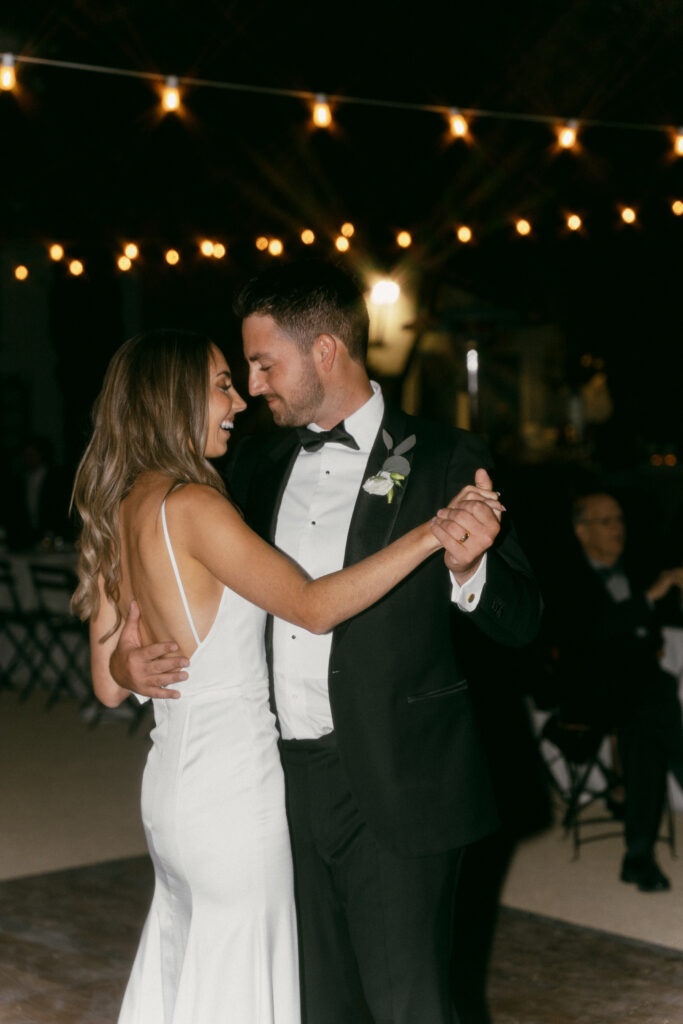 bride in modern minimalist wedding dress and groom in classic black tuxedo suit have first dance