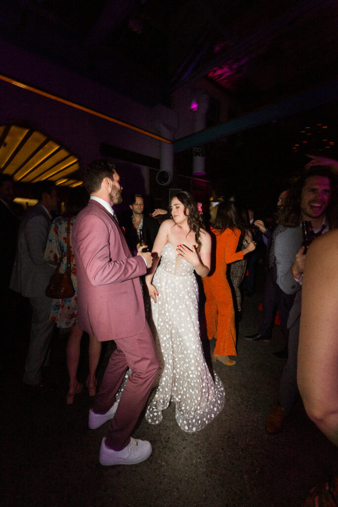 bride in strapless wedding dress with sweetheart neckline and groom in merlot colored suit with floral tie dance with guests