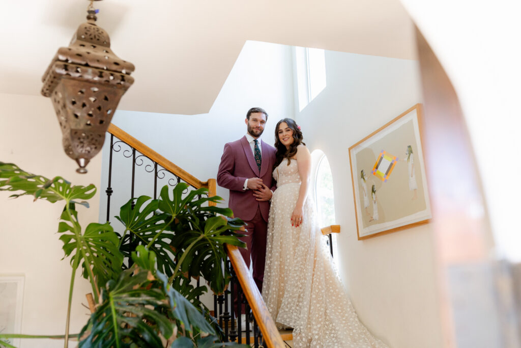 bride in strapless wedding dress and groom in merlot suit on staircase