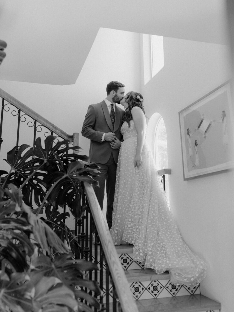 bride in strapless wedding dress and groom in merlot suit on staircase