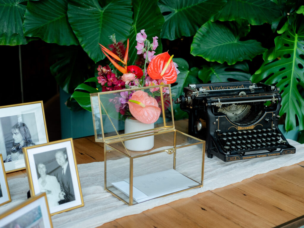tropical inspired floral centerpiece on welcome table with gold framed card box and vintage typewriter