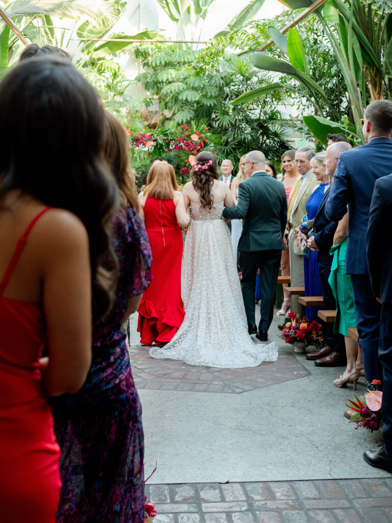 bride in strapless wedding dress and tropical inspired floral bouquet walks down ceremony aisle