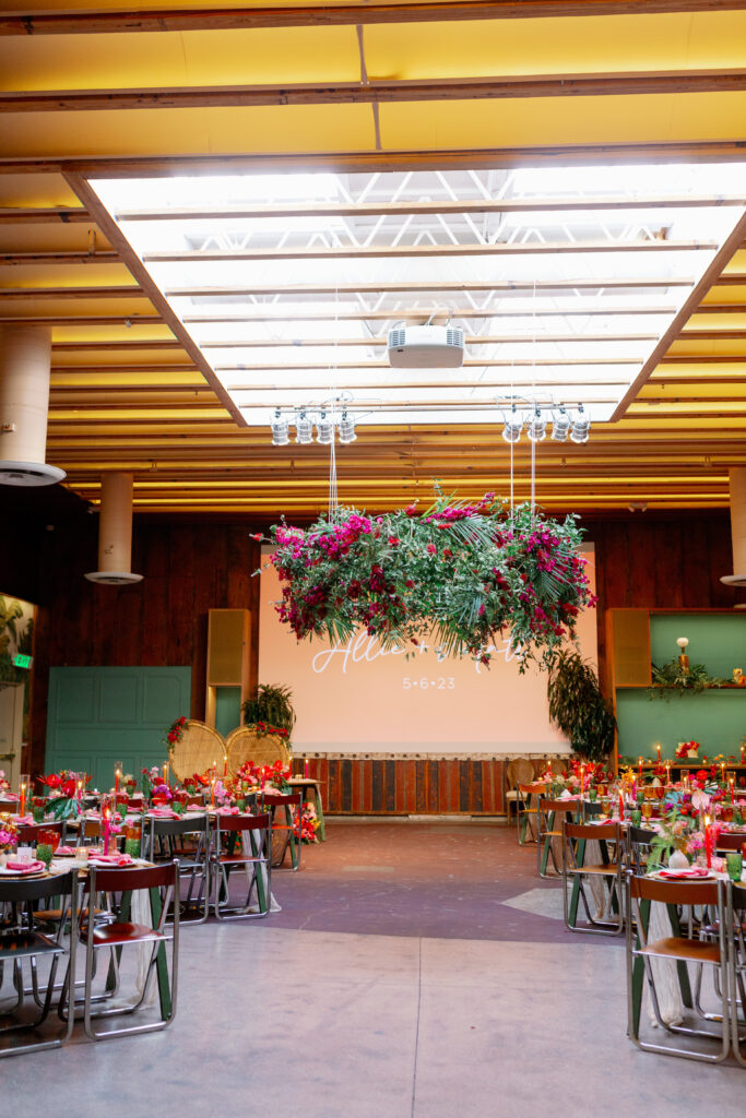 tropical inspired wedding reception with large hanging floral installation and brightly colored table settings and unique floral arrangements