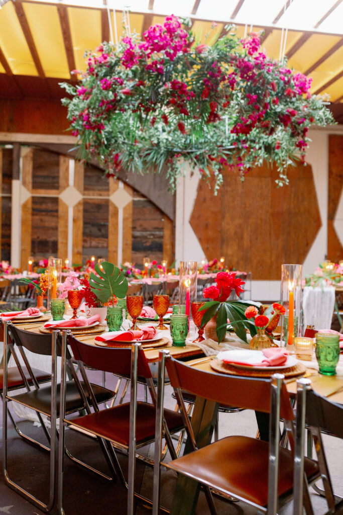 tropical inspired wedding reception with large hanging floral installation and brightly colored table settings and unique floral arrangements