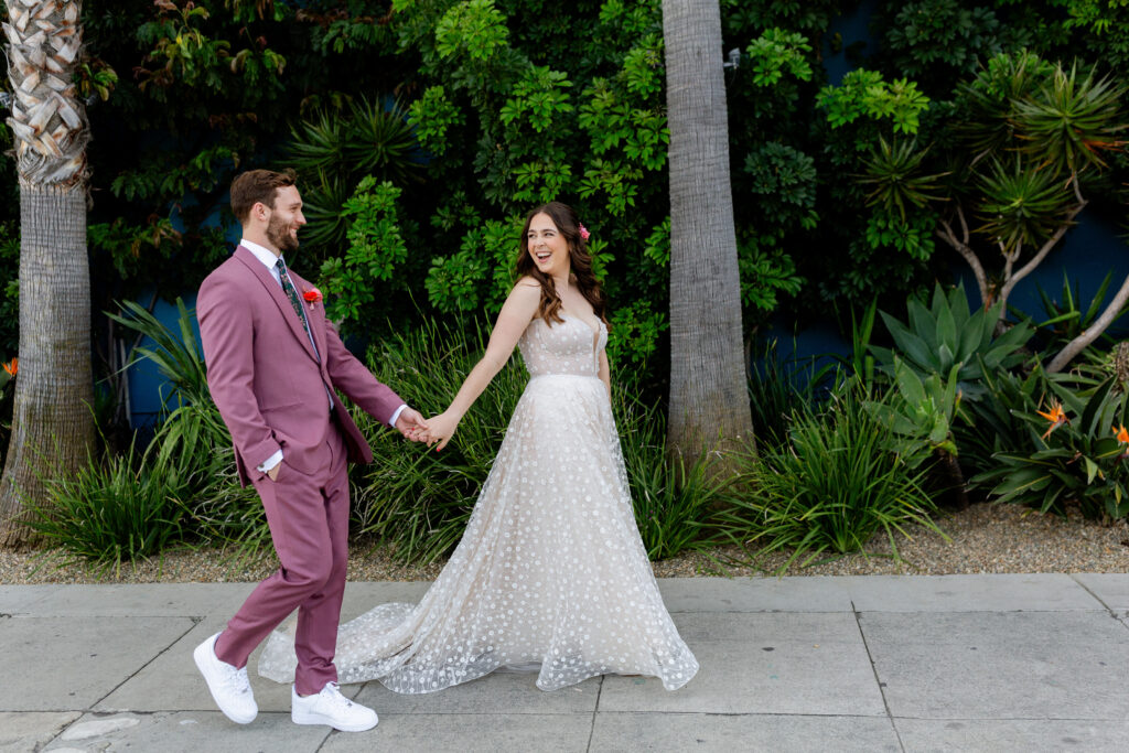 bride in strapless wedding dress with sweetheart neckline and groom in merlot colored suit with floral tie take portrait photos in downtown Los Angeles