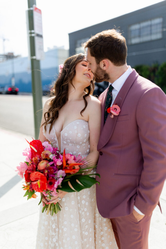 bride in strapless wedding dress with sweetheart neckline and groom in merlot colored suit with floral tie take portrait photos in downtown Los Angeles
