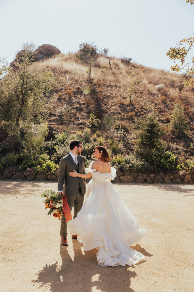 bride in modern off shoulder ruffled wedding dress with a high slit and groom with glasses and warm grey suit during portrait shots