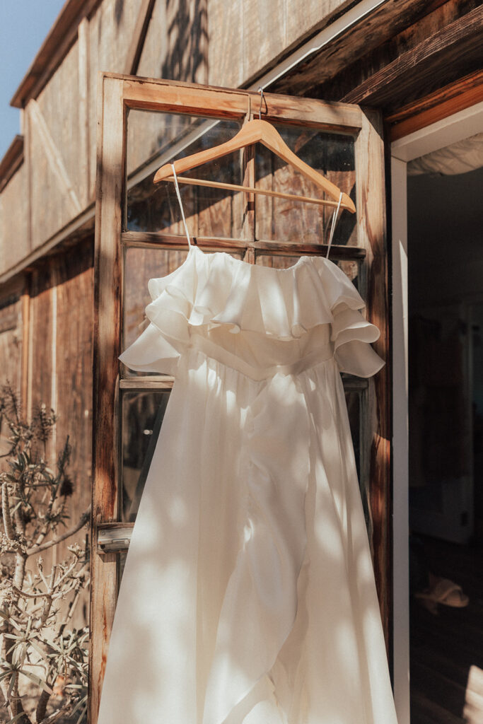 modern asymmetrical off-shoulder wedding dress hanging from door