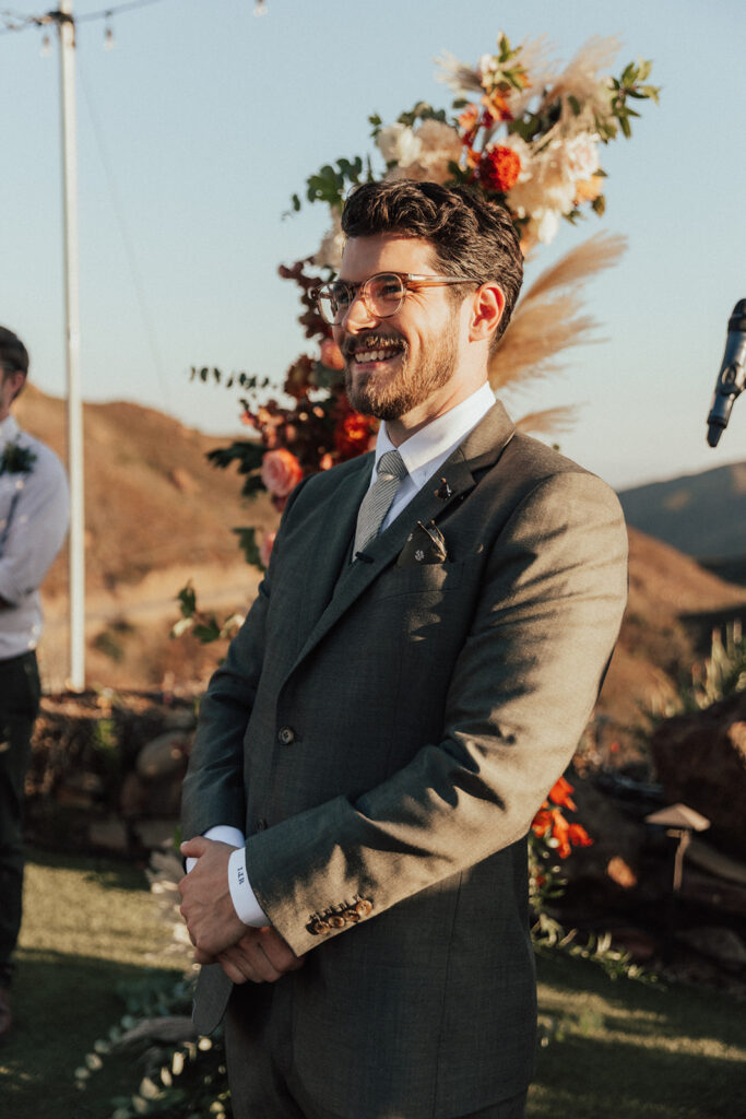 groom with glasses wearing warm grey suit during wedding ceremony