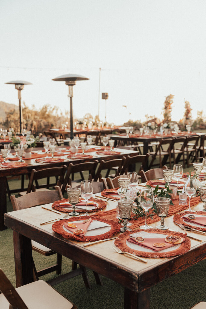 fall wedding reception tables with wooden farmhouse tables and burnt orange chargers, napkins and citrus slice garnish 