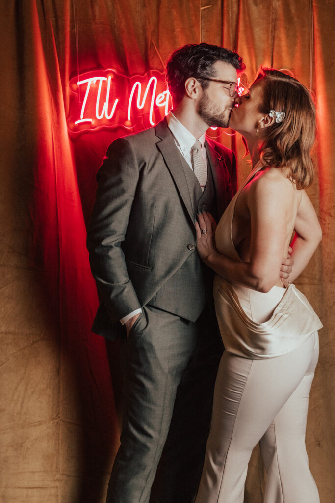 bride in modern wedding reception jumpsuit with groom take photos with neon letter back drop