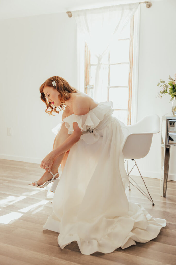 bride in modern asymmetrical off shoulder wedding dress and classic hollywood bridal look with soft waves and red lip 
