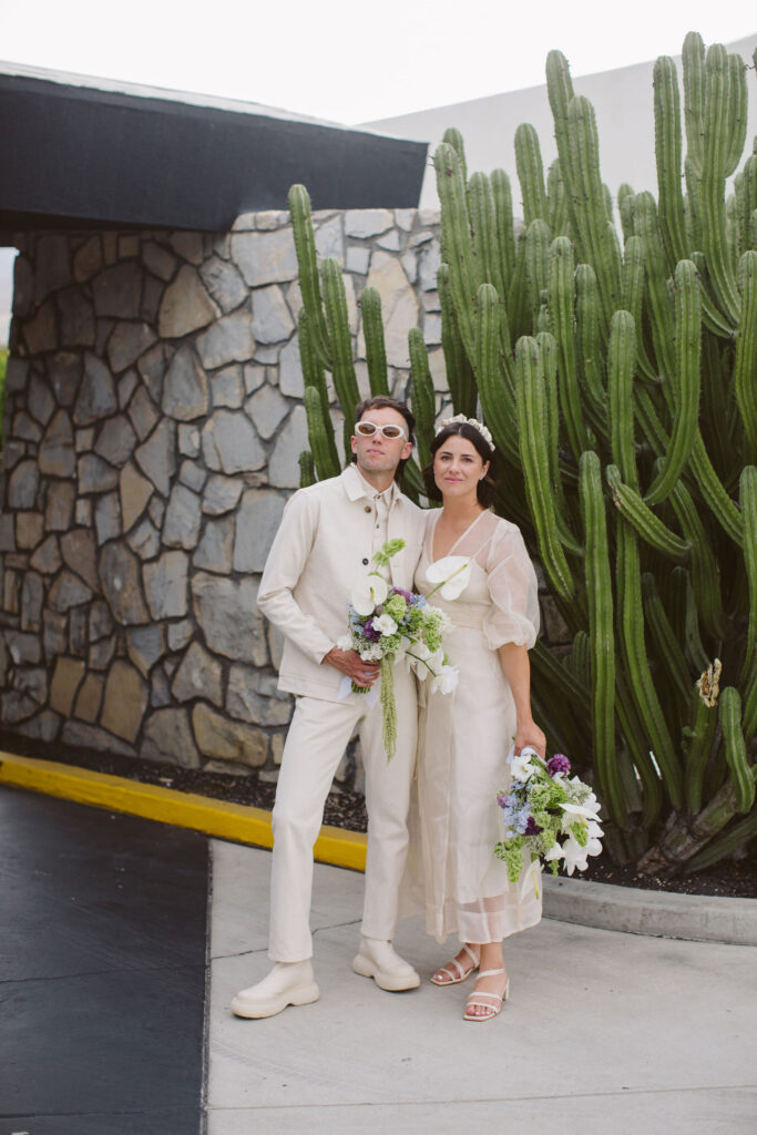 portraits of bride in modern wedding dress with sheer overlay and satin headband and groom in all white outfit with both holding bouquets