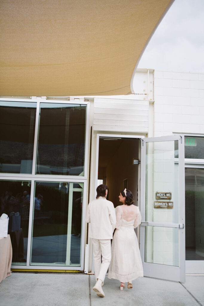 bride in modern wedding dress with sheer overlay and groom in all white wedding outfit walk together after wedding