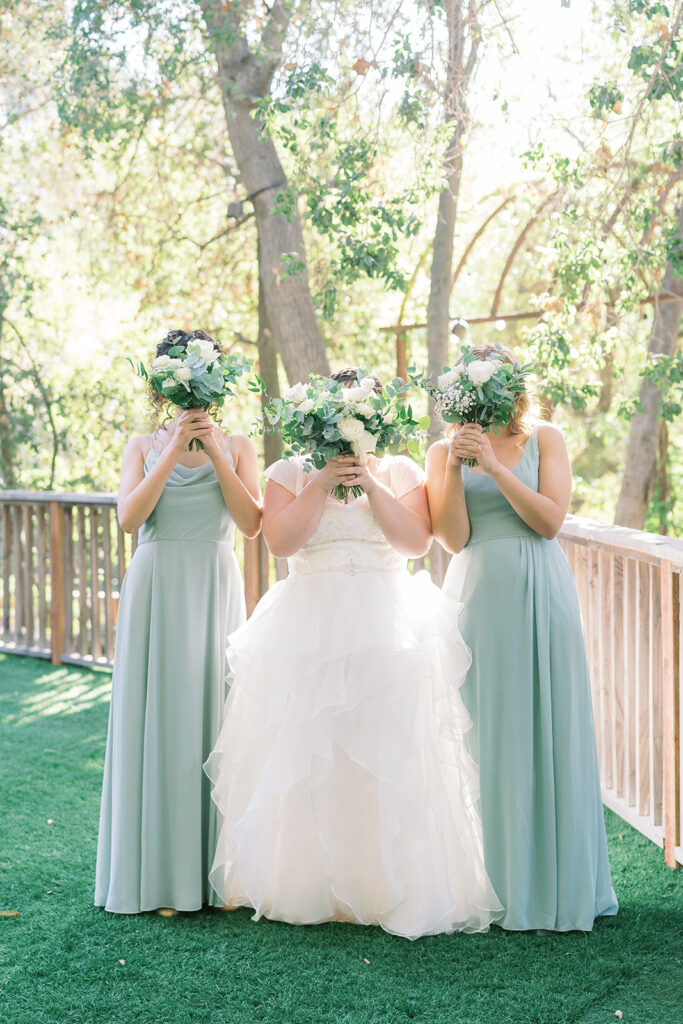 bride in organza ballroom wedding dress with bridesmaids in soft teal dresses holding up bouquets