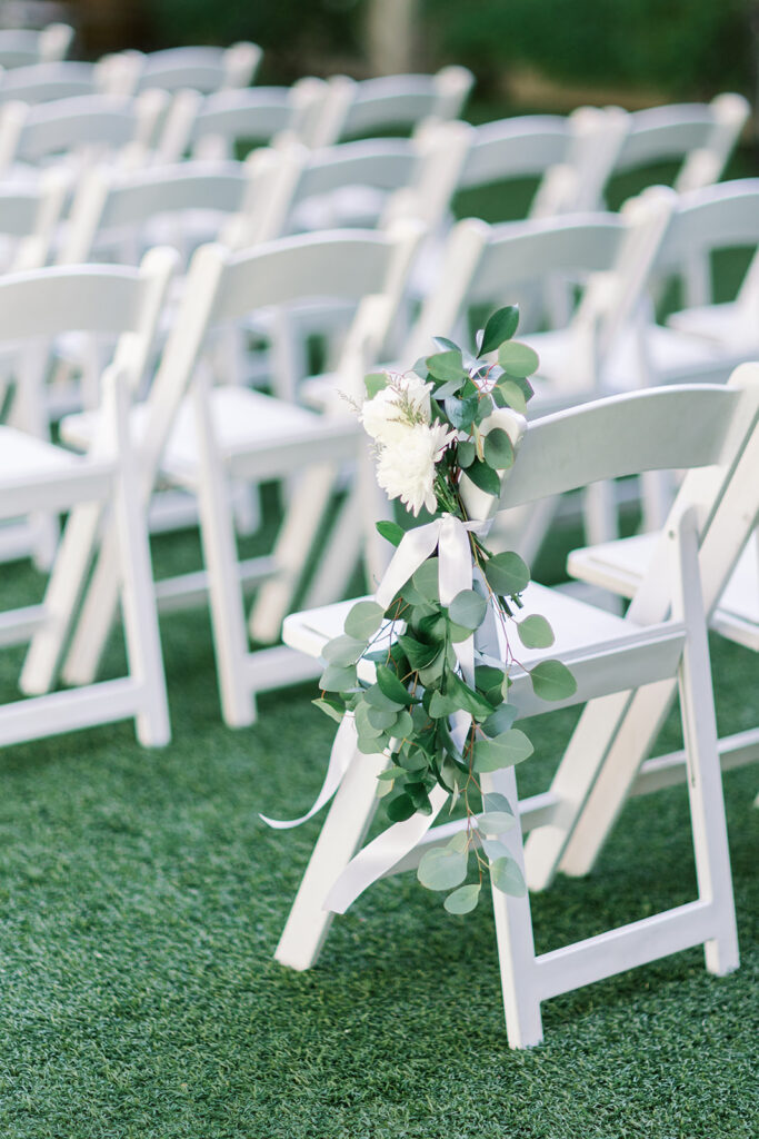white wedding ceremony chairs with flowers attached 
