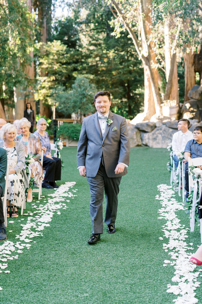 groom walks down the aisle during light and airy wedding ceremony at Calamigos Redwood Room with white drapery and flowers