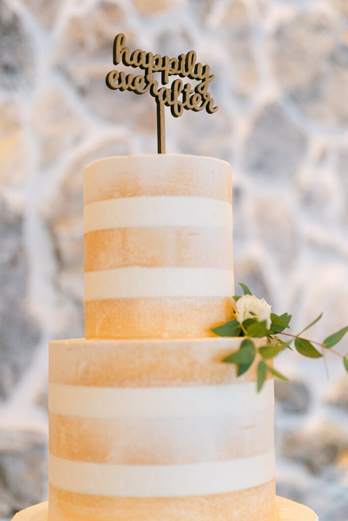 wooden happily ever after cake topper on top of naked wedding cake