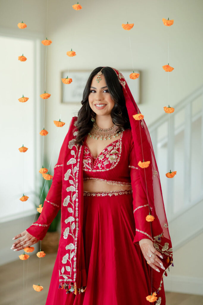 bride in red sari surrounded by hanging marigolds