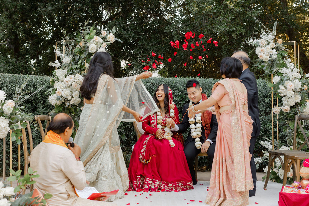 bride in red saari and groom in black tuxedo sprinkled with rose petals during wedding ceremony at Maravilla Gardens