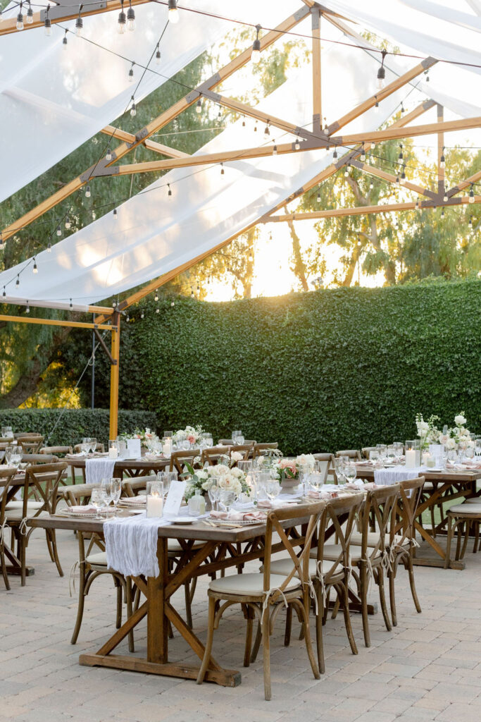 soft outdoor wedding reception with pink and white florals, pillar candles and gauze table runner on wooden farmhouse tables and wooden chairs at Maravilla Gardens in Los Angeles