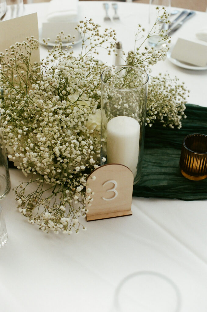 wooden table number on minimalist yet refined wedding reception at Calamigos Ranch with green gauze table runner, candles and baby's breath floral arrangements